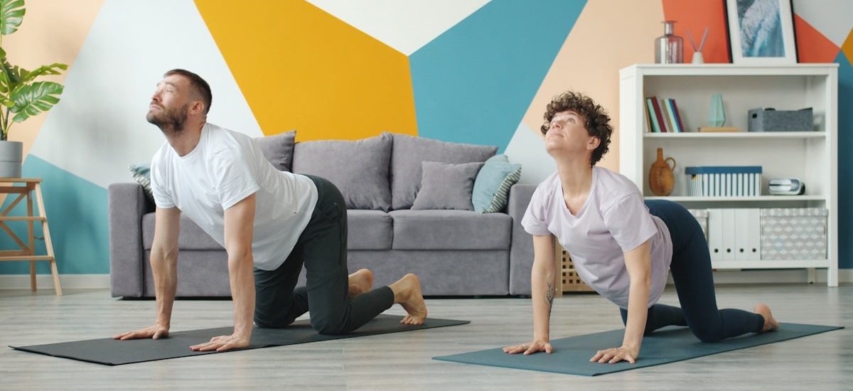 Slow motion of young attractive husband and wife doing yoga in apartment together caring for health training body. Cozy room is visible in background.
