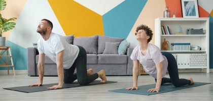 Slow motion of young attractive husband and wife doing yoga in apartment together caring for health training body. Cozy room is visible in background.