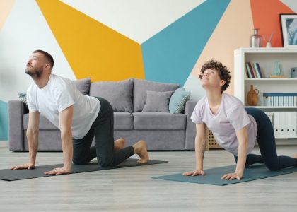 Slow motion of young attractive husband and wife doing yoga in apartment together caring for health training body. Cozy room is visible in background.
